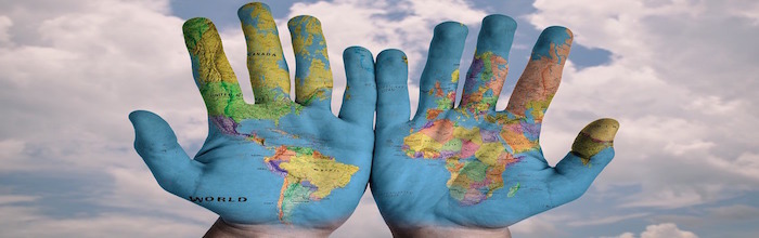 World map painted on two hands against sky background