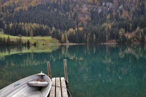 Small metal boat tied to a dock on a lake next to tree-covered cliff