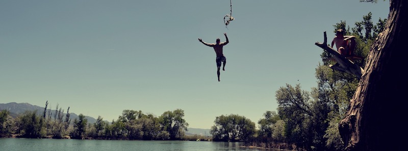 Man jumping off rope swing into a river